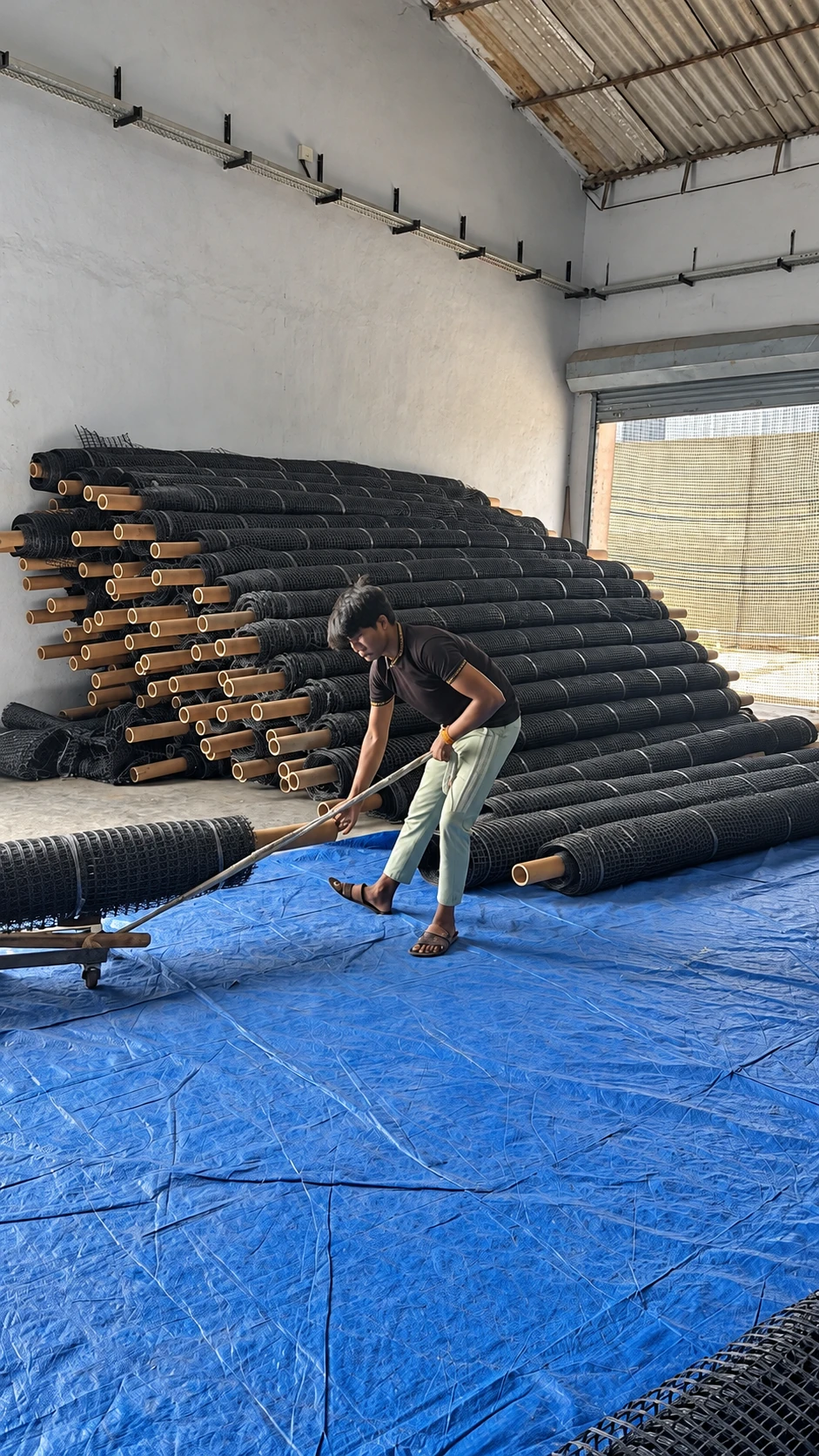 Workplace view with stacked geogrid rolls and a roll being handled